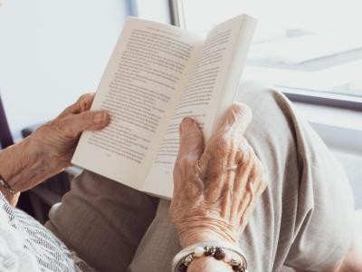 Seniorin hält ein Buch in den Händen.
