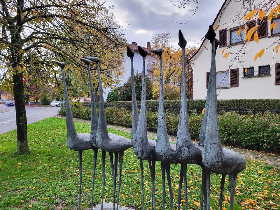 9 nebeneinander stehende Vögel aus Bronze.