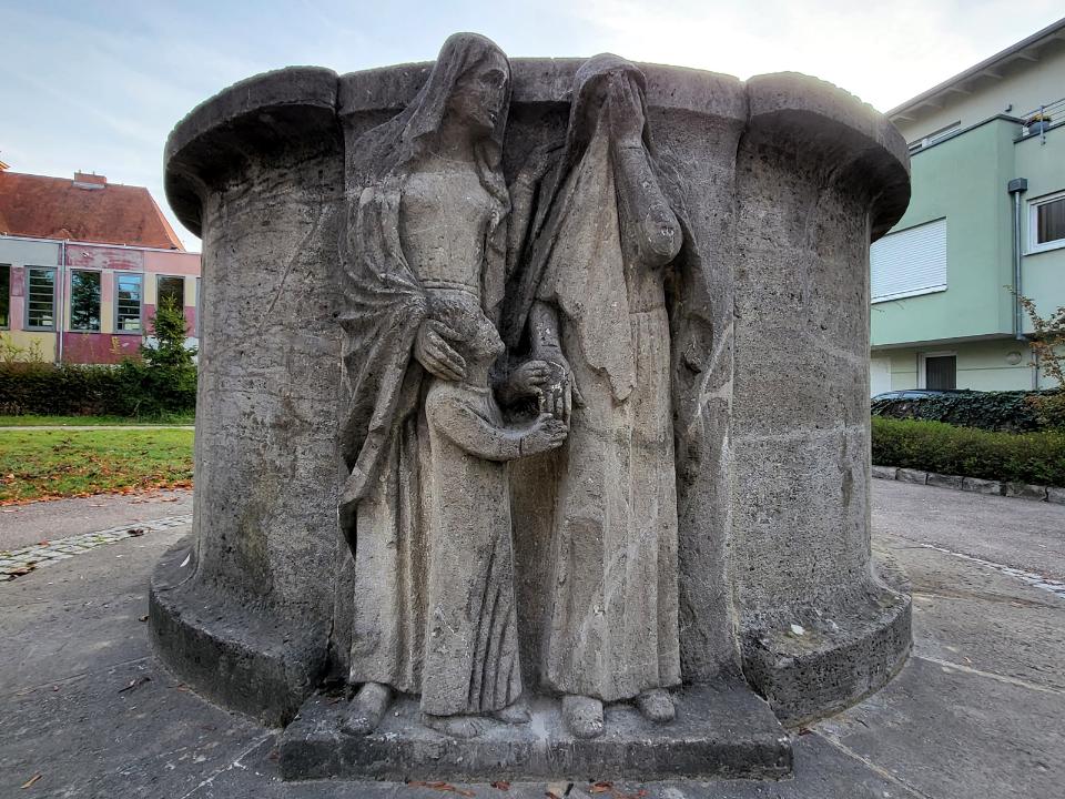 Graue Brunnenschale mit Relief von zwei trauernden Frauen mit Kind.