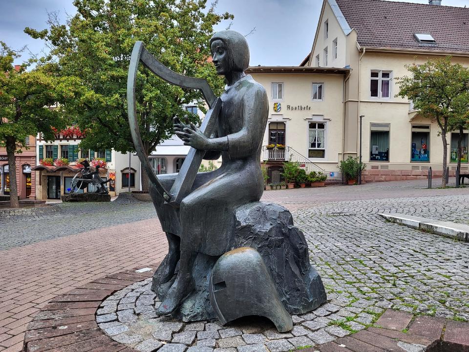 Sitzende männliche Figur aus Bronze spielt auf einer Leier.