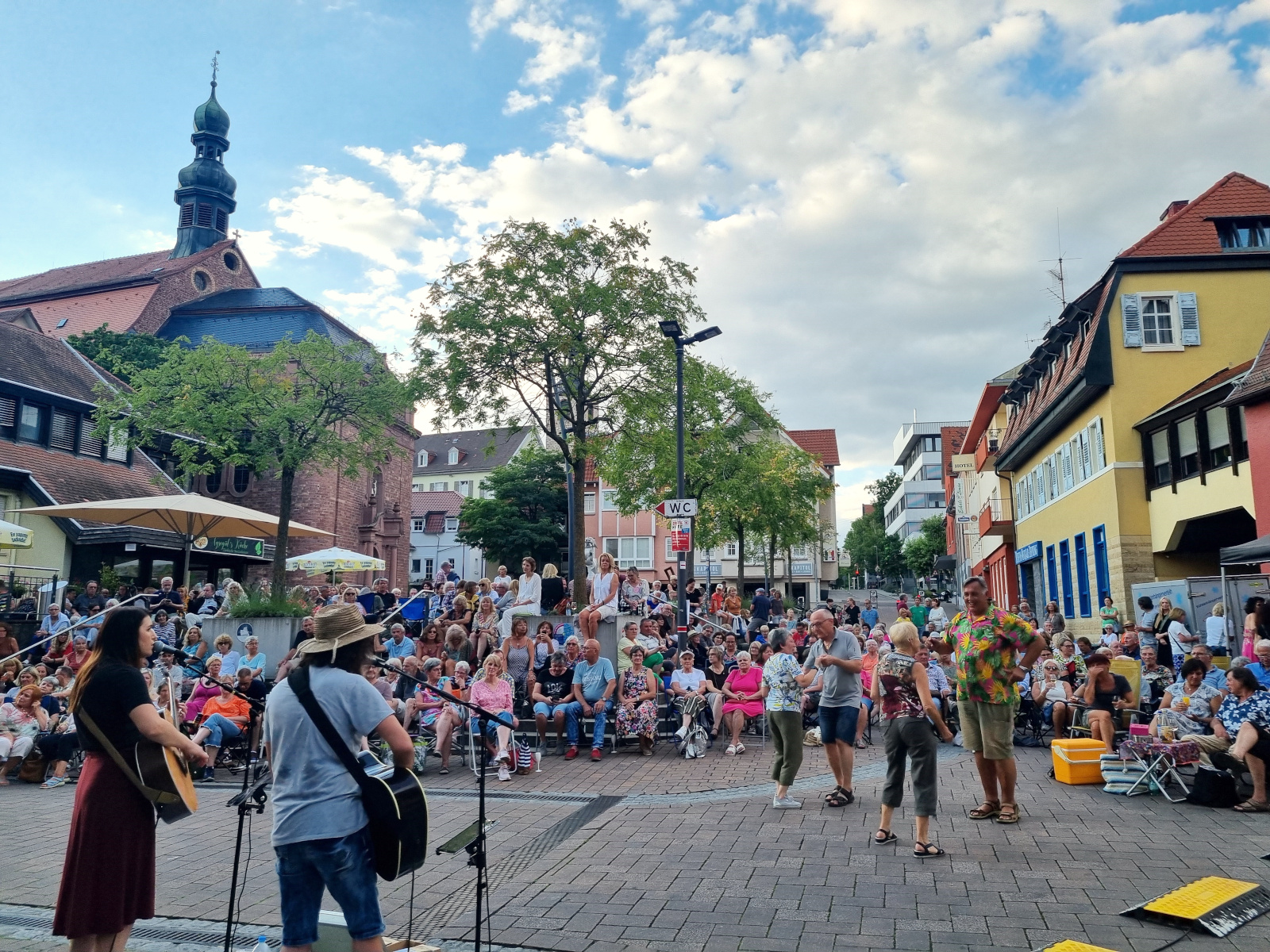 Konzert am Adenauerplatz, viele Menschen sitzen auf ihren mitgebrachten Klappstühlen..