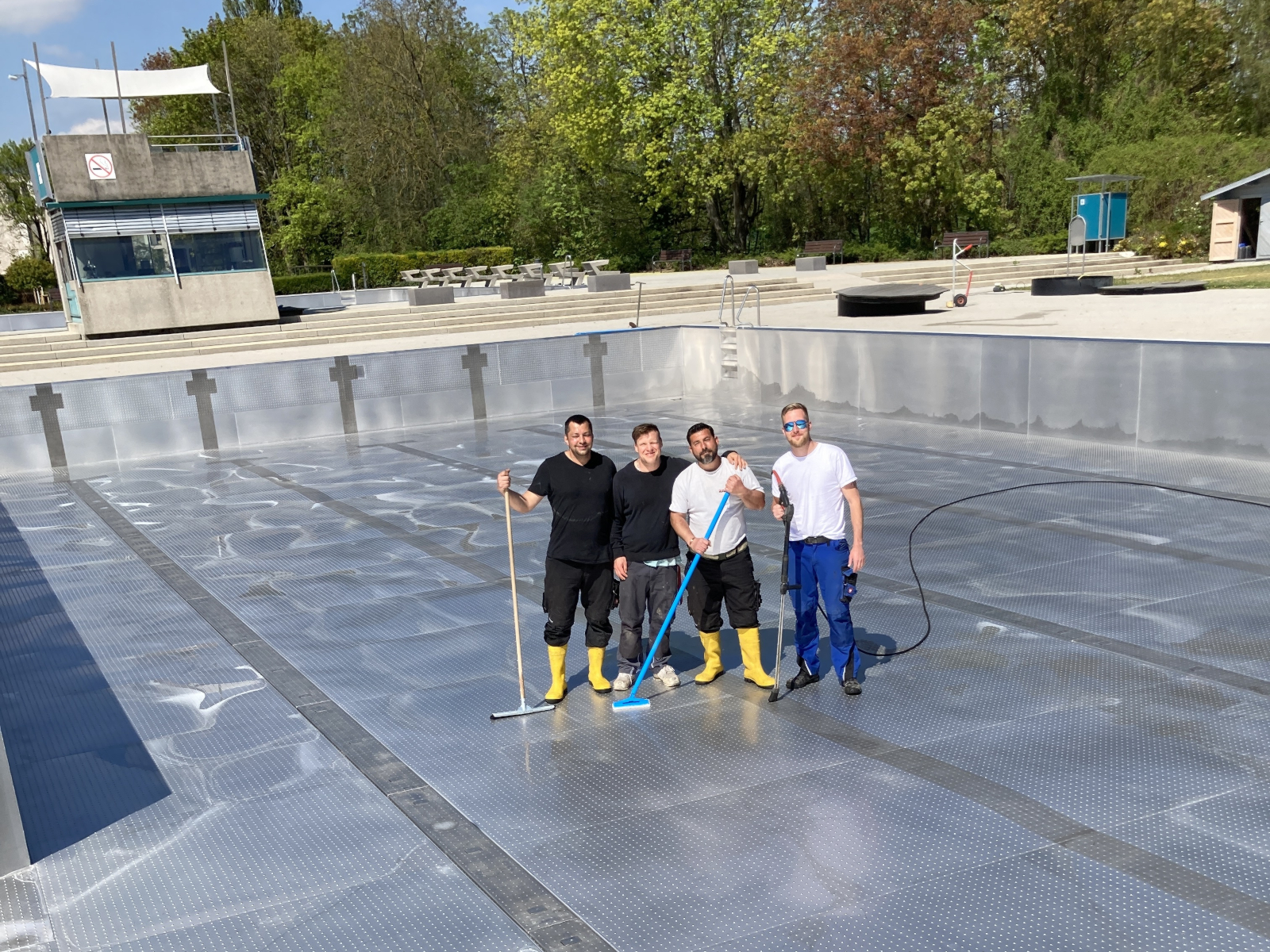 Mitarbeitende der Stadtwerke Wiesloch sehen in einem leeren Schwimmbecken, mit Reinigungsutensilien.